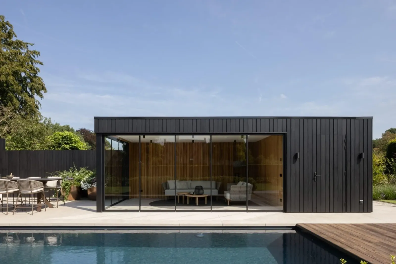 Zwart houten poolhouse van Bronkhorst aan het zwembad, in de zon